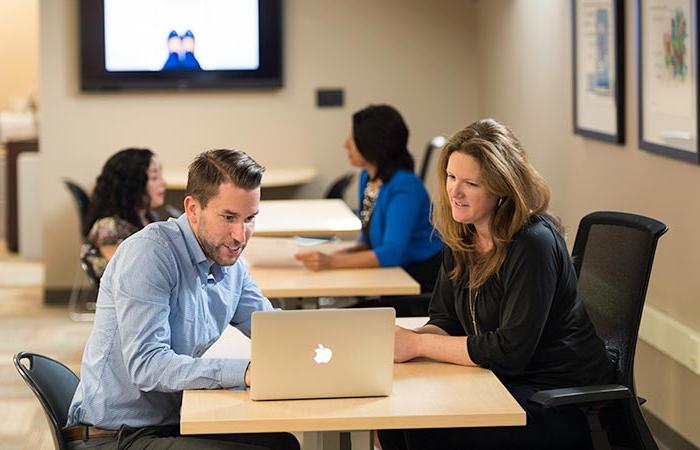 A man and a woman meeting at a table and looking at a computer.