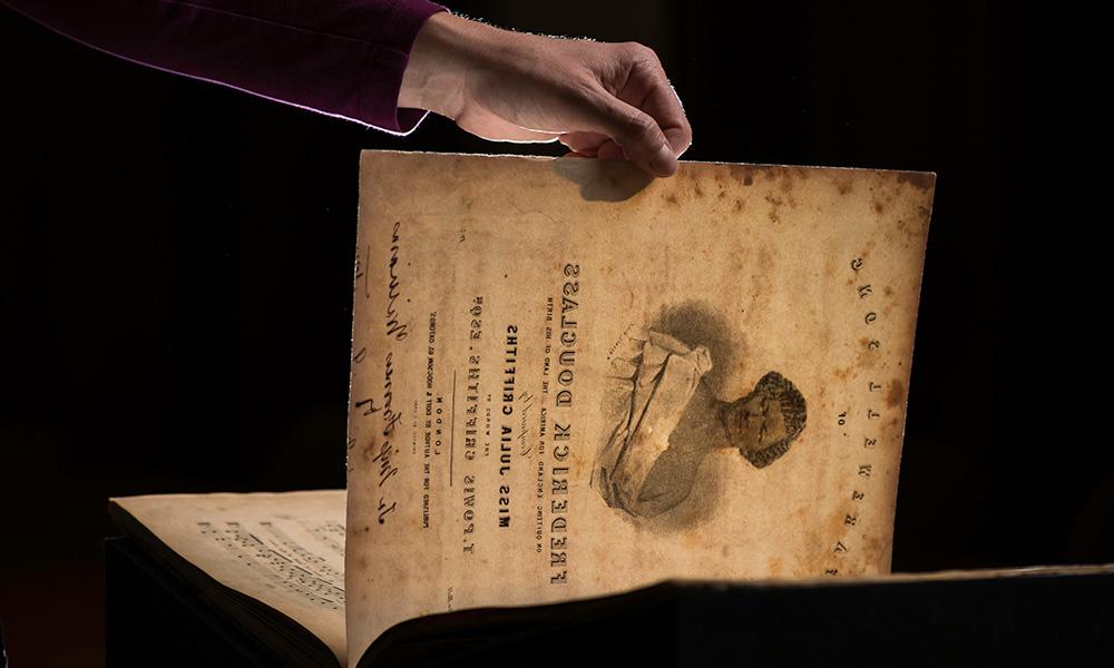 hand holding a piece of sheet music bearing the image and name of Frederick Douglass