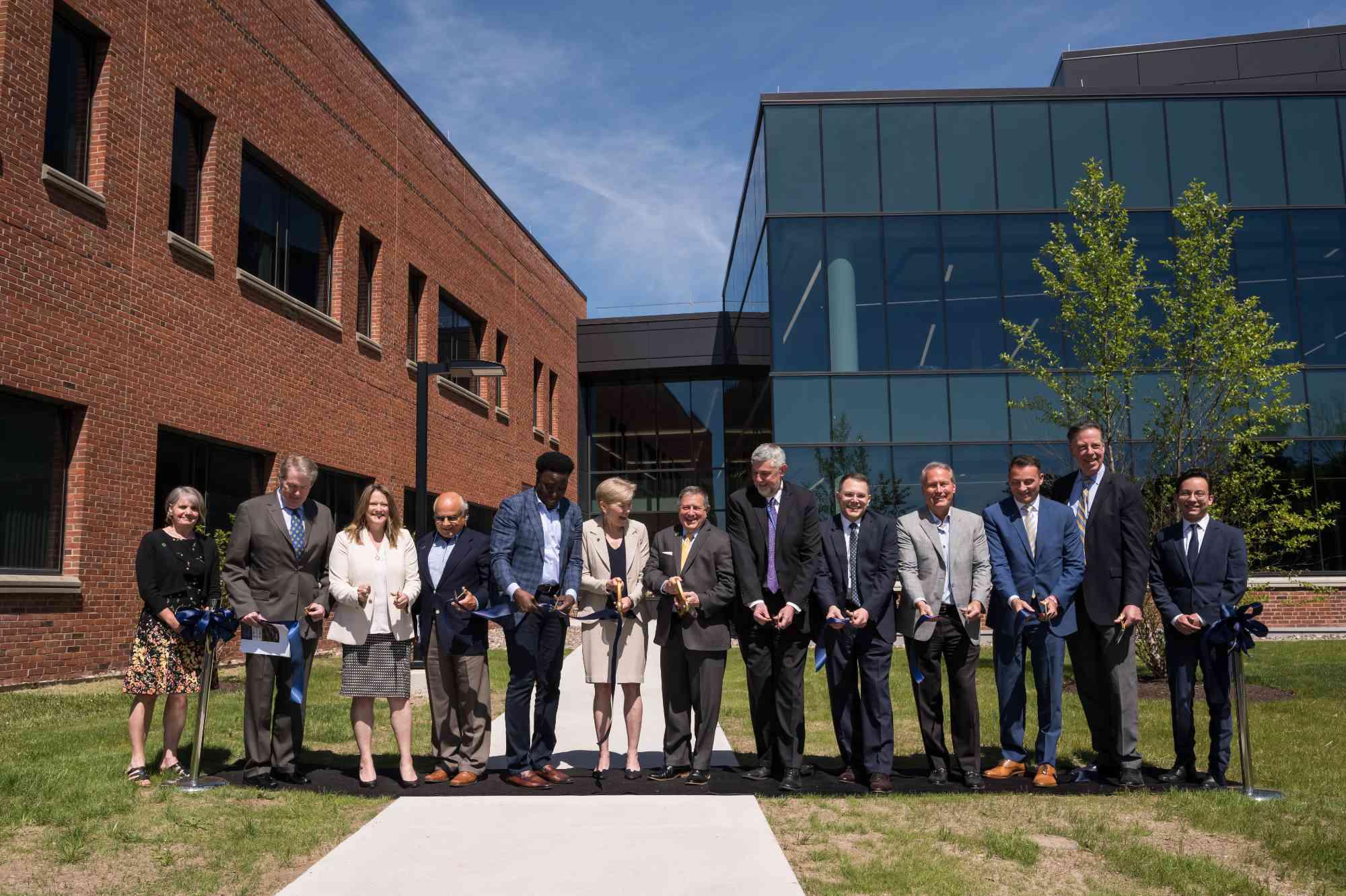 Group of about a dozen people standing in front of the LLE building expansion getting ready to cut a ribbon.