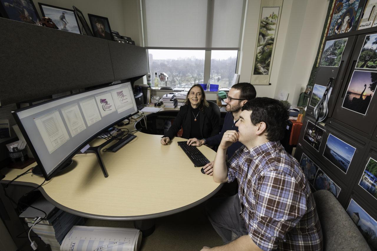 A University of Rochester professor and two students in an office, sitting around a computer with a complicated data set on it