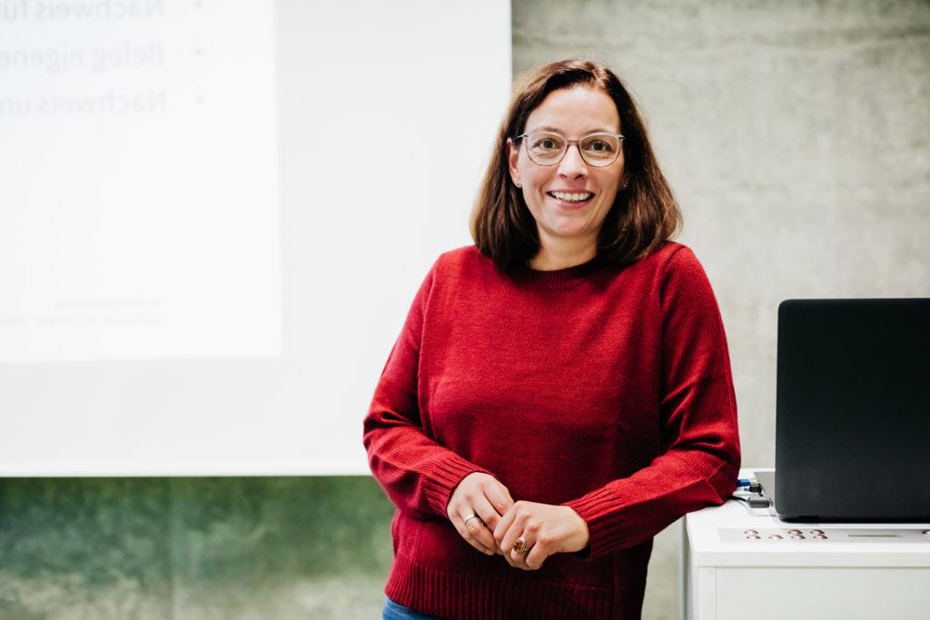 A professor standing at the front of her classroom in front of a chalk board